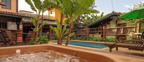 A hot tub area with a pool, wooden lounge chairs, and a tropical setting with banana trees.