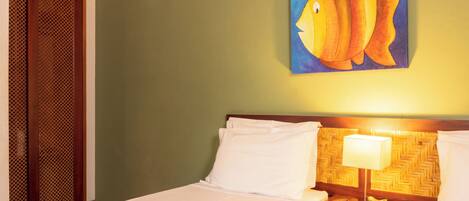 Ein Hotelzimmer mit einem Bett, einem Nachttisch mit Lampe, einem Wandbild von einem Fisch und einer Holztür mit Netzmuster.