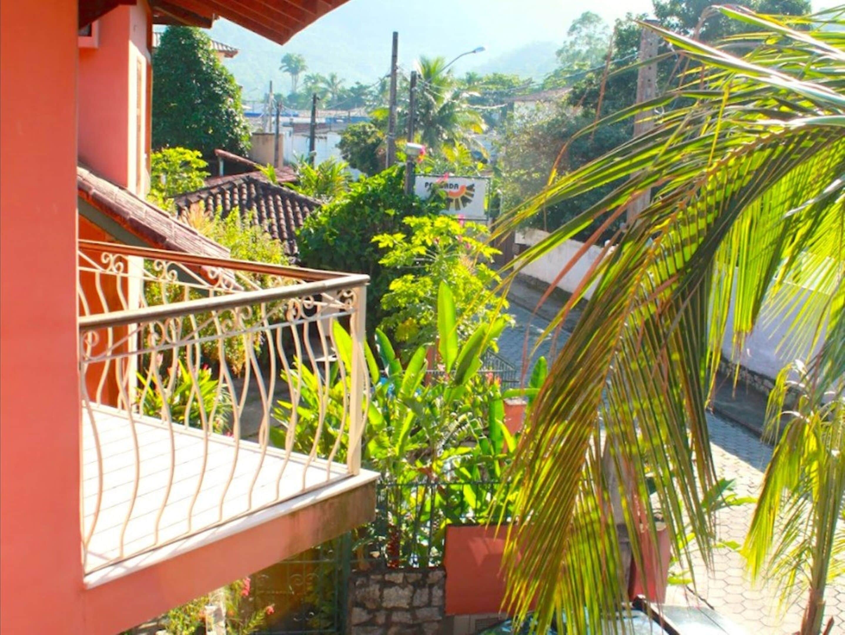 A balcony with a wrought iron railing, surrounded by lush greenery and a view of a river.