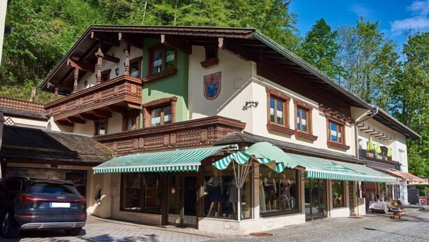 A traditional building with a balcony, a shop with a striped awning, and a car parked in front. - Apartment Jenner, 1-4 persons, 135 sqm, 1 bedroom, terrace, near Königssee (Schönau am Königssee)