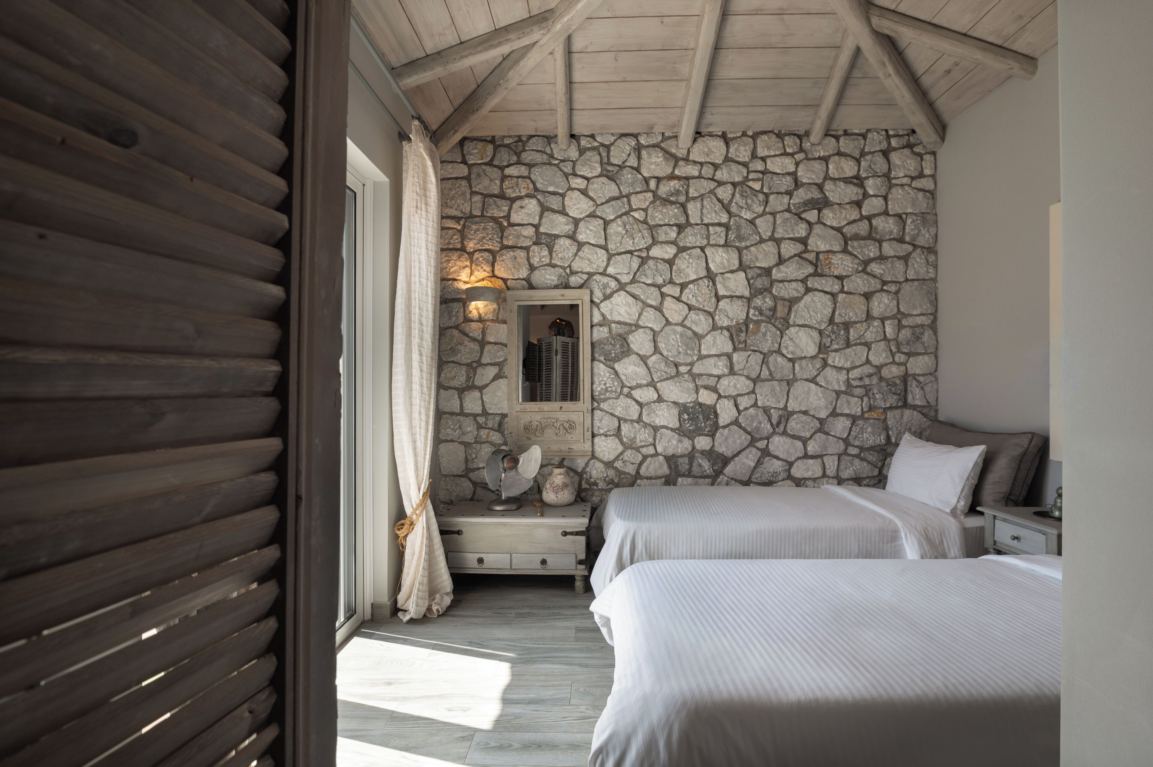 A bedroom with two beds, a stone wall, a mirror, and a wooden ceiling.