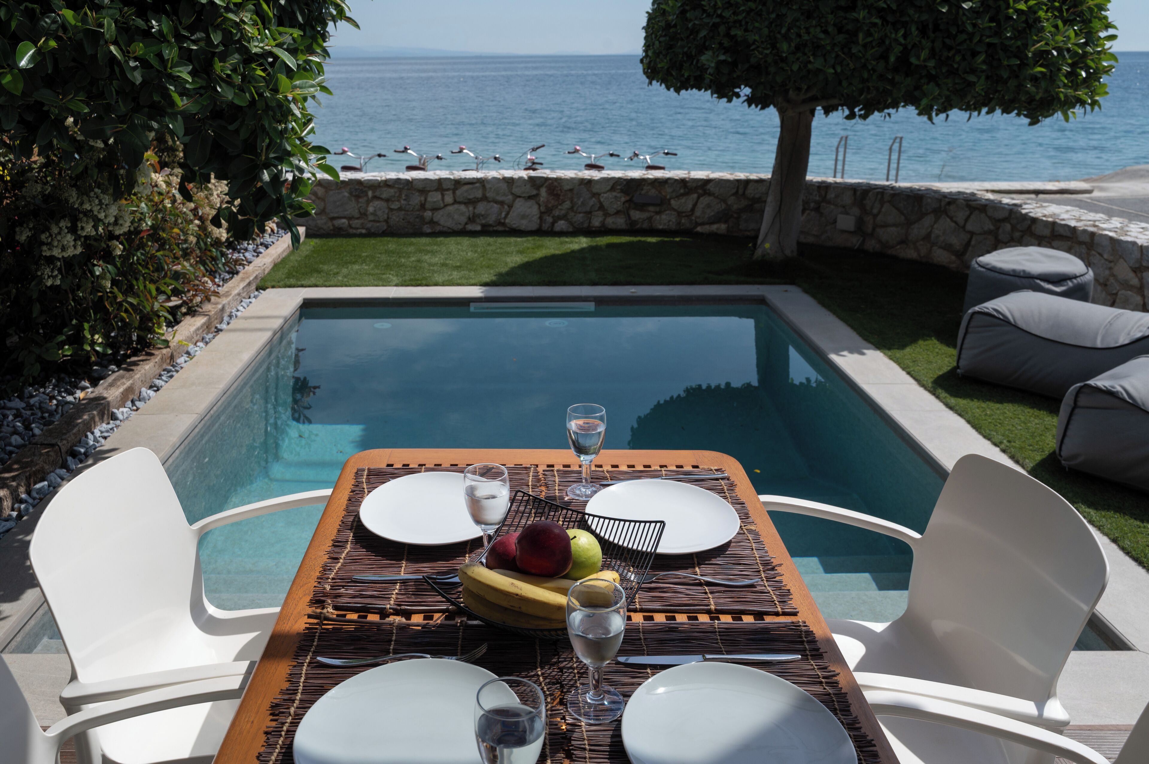 A poolside dining setup with a table, chairs, and a view of the sea.