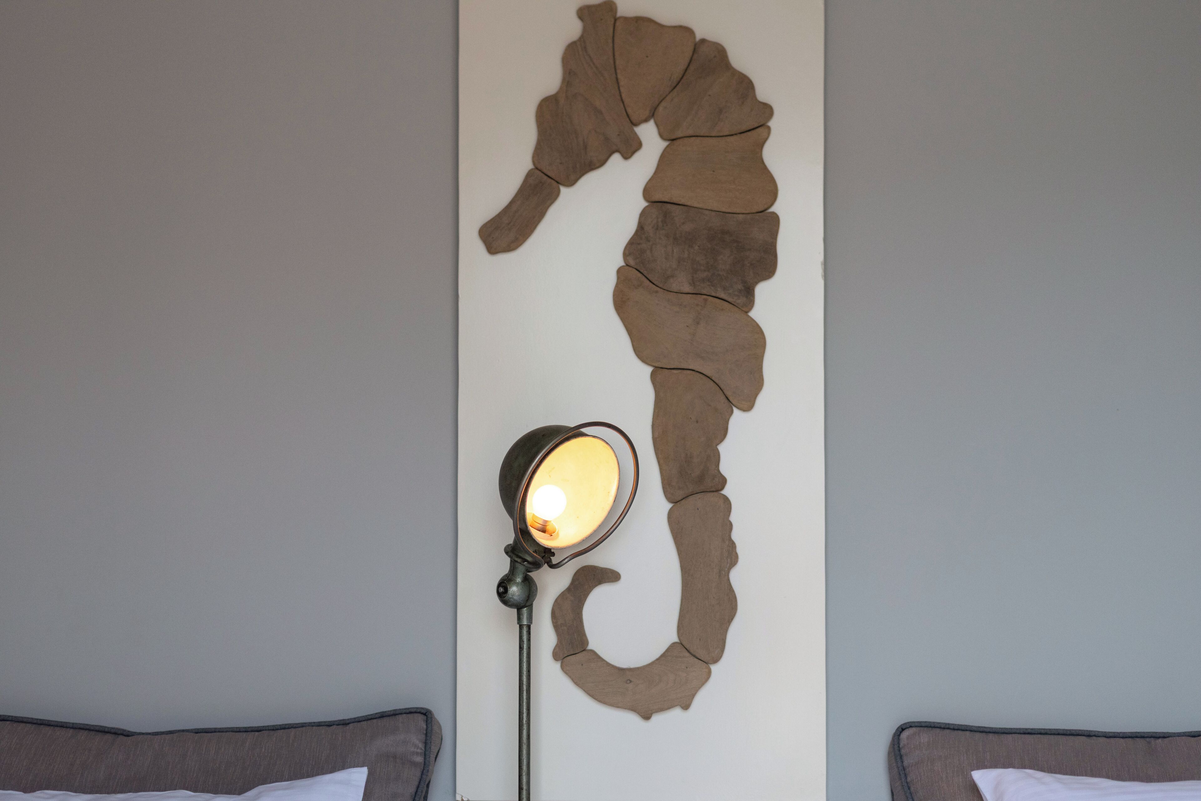 A room with a unique wall art piece resembling a segmented snake, a floor lamp, and two beds.