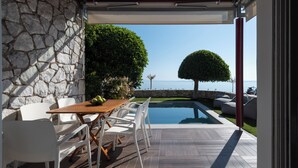 Un patio con mesa y sillas, piscina y vista al mar.