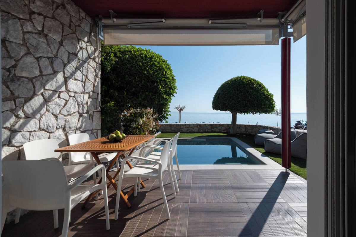 Un patio con mesa y sillas, piscina y vista al mar.
