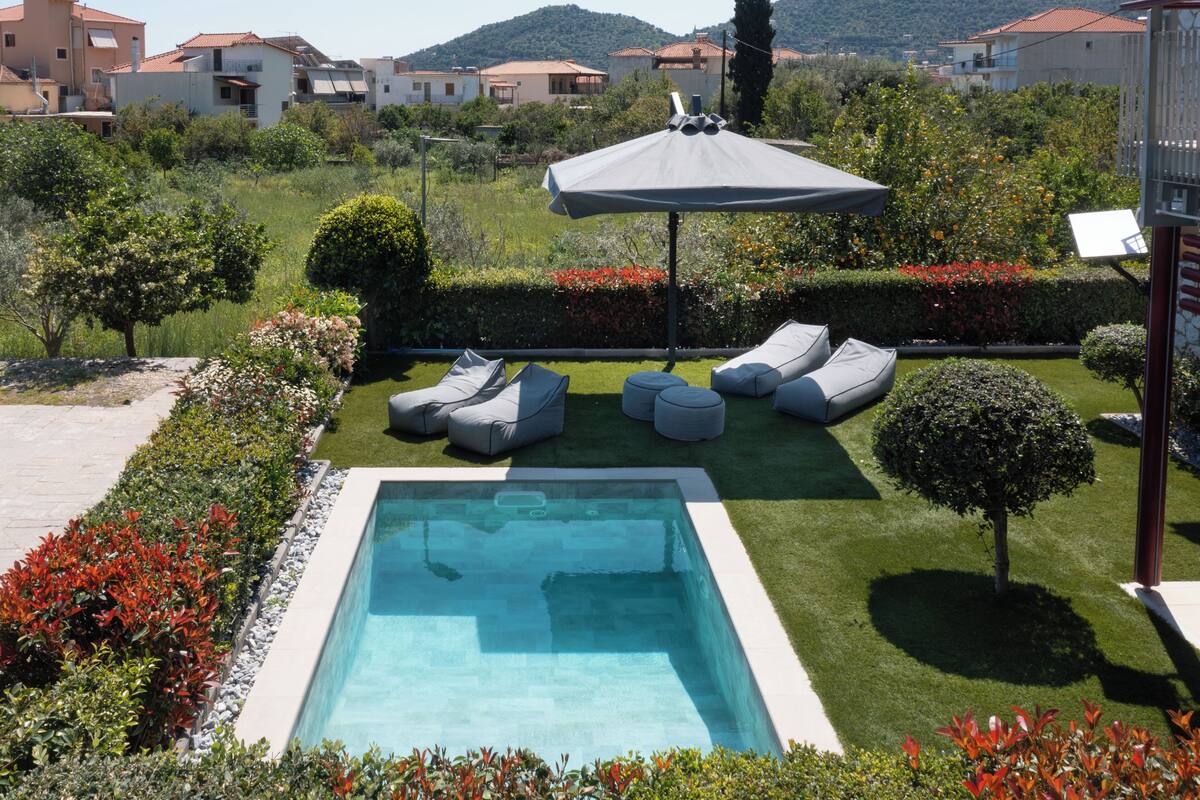 Una piscina con sillas de descanso, un pequeño jardín y vistas a casas vecinas.