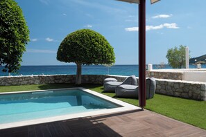 Una piscina con un muro de piedra, un árbol podado y vistas al mar.
