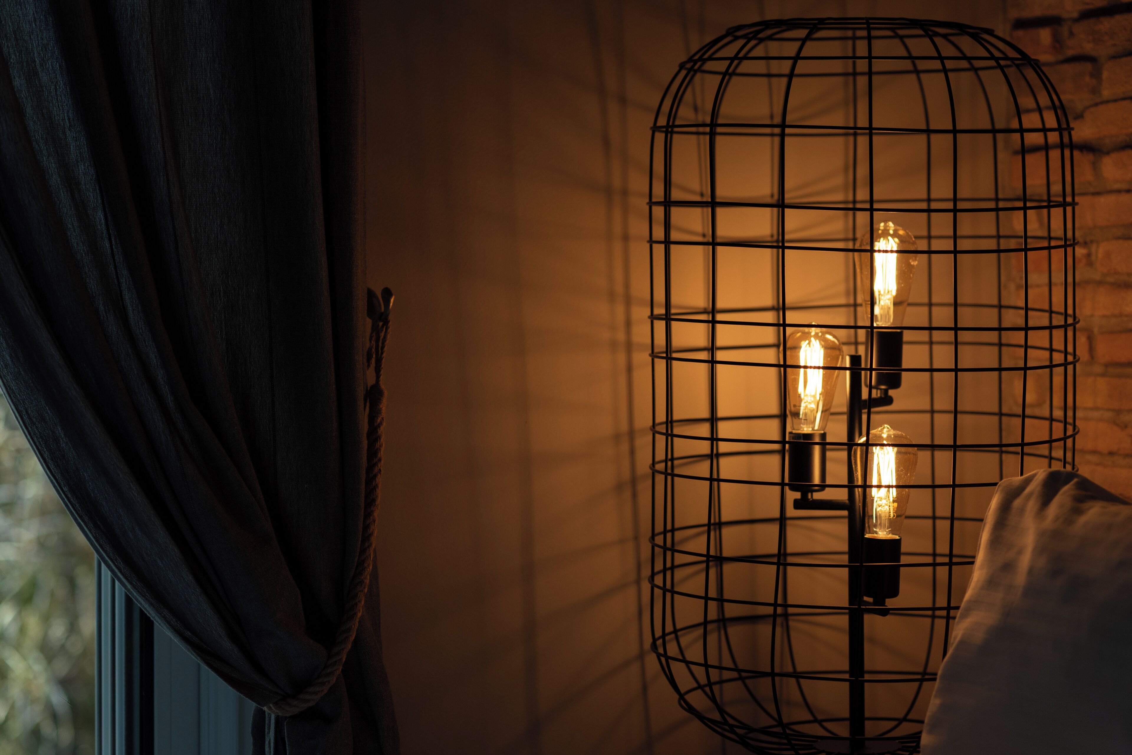 Een kamer met een raam, een gordijn en een wandlamp met blootliggende lampen.