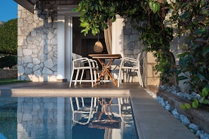 Zona junto a la piscina con paredes de piedra, una mesa y sillas.