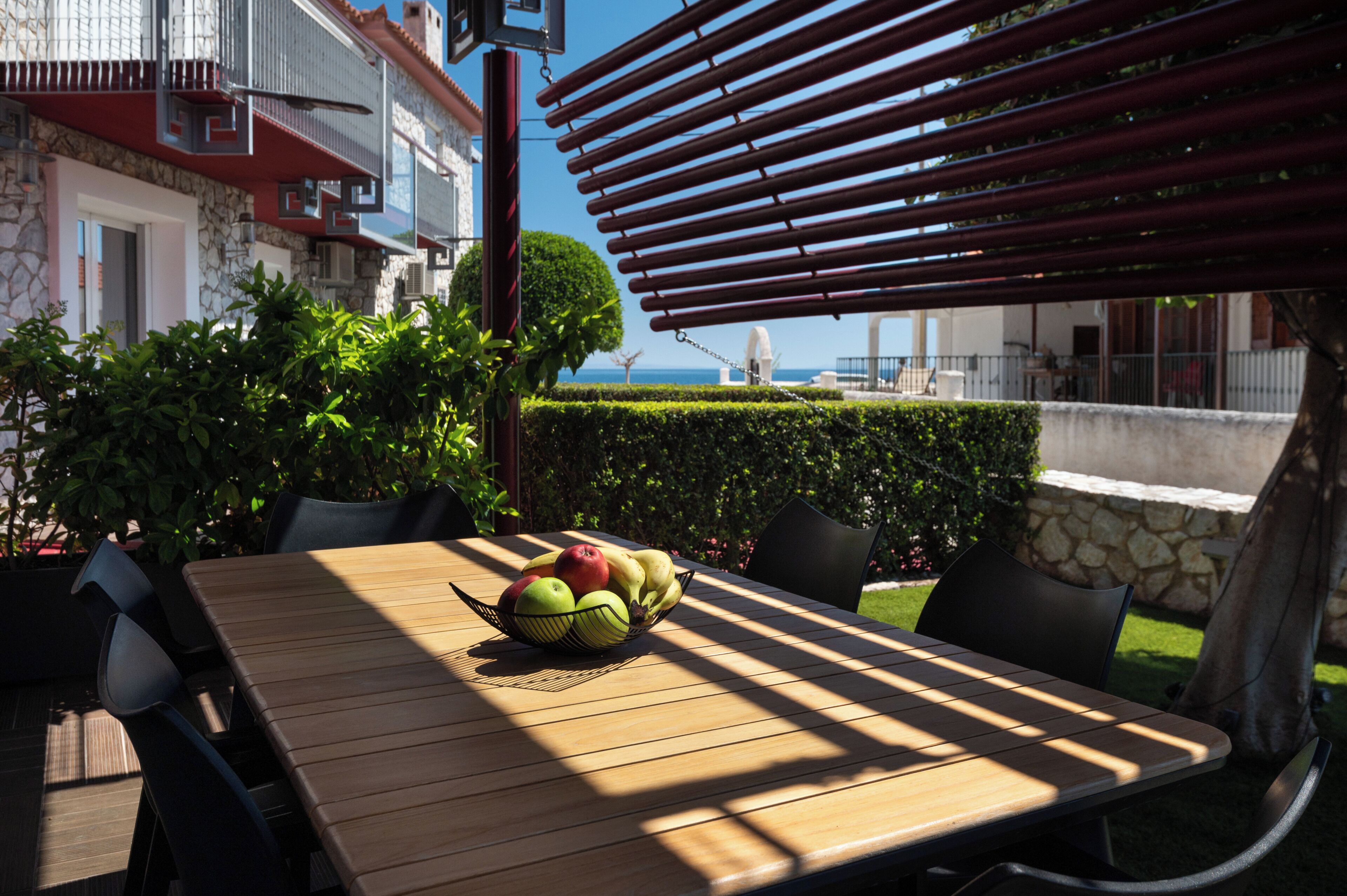 Un espace extérieur aménagé pour prendre les repas, avec une table, des chaises et un saladier rempli de fruits.