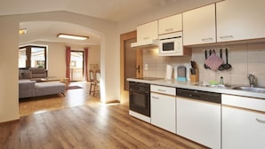 Une cuisine moderne avec des meubles blancs, un four à micro-ondes et un lave-vaisselle. Le sol est en bois et la pièce offre une vue sur le salon, qui comprend un canapé et un coin repas.