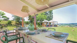 Een terras met eethoek, een tafel gedekt voor twee personen, omringd door groene stoelen, een decoratieve vaas met bloemen en uitzicht op het platteland.