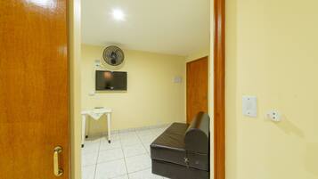 Een kamer met een bed, een bureau, een televisie en een ventilator.