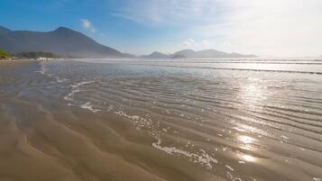 Una playa con olas suaves y montañas al fondo.