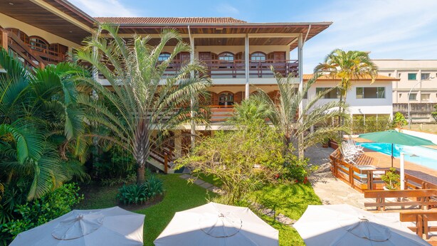 A hotel courtyard with a pool, outdoor seating, and lush greenery. - Chalés Four Seasons (Ubatuba)