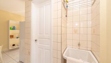 Un baño con una puerta blanca, una bañera y un estante con artículos de aseo.