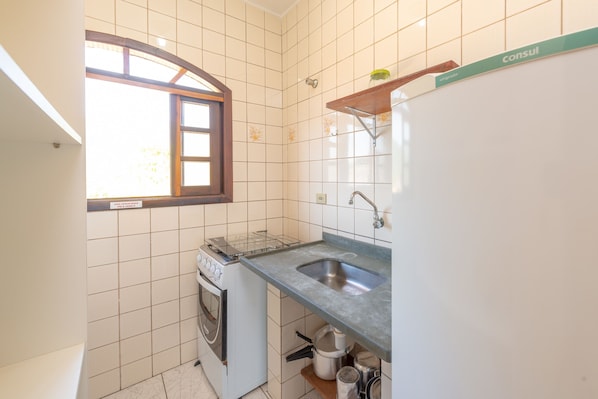 A small kitchen with white tiles, a window, a sink, and a stove. - Chalés Four Seasons (Ubatuba)