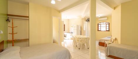 A hotel room with two single beds, a dining area with a table and chairs, a ceiling fan, and a view of the kitchen and bathroom through an open door.