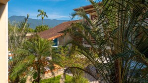 A view of a building with a red-tiled roof, surrounded by palm trees and greenery, with mountains in the background. - Chalés Four Seasons (Ubatuba)