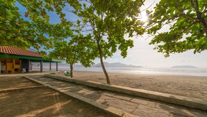 A beachside view with a covered seating area, a concrete pathway, and a view of the ocean and distant mountains. - Chalés Four Seasons (Ubatuba)