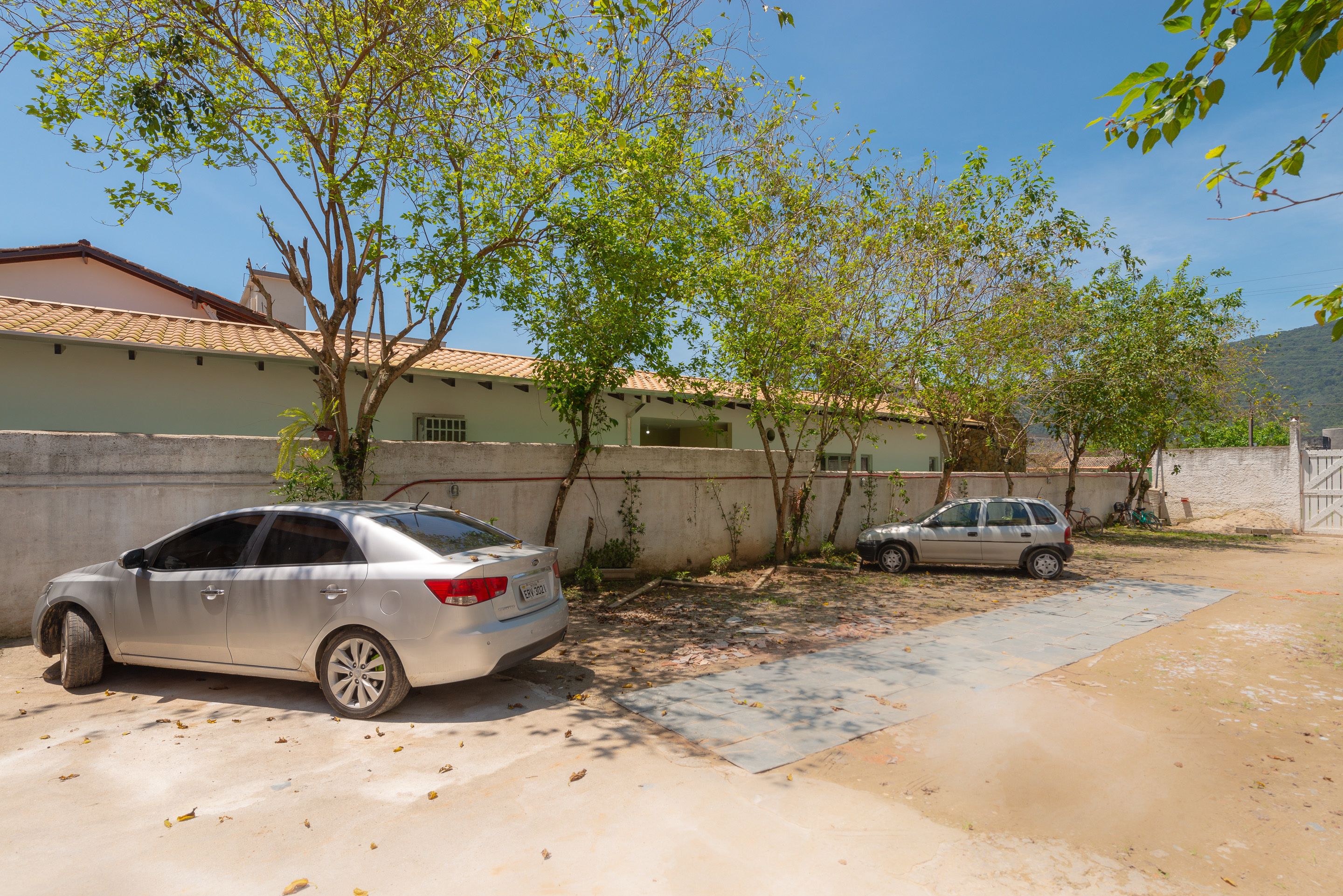 A residential area with two parked cars, a concrete wall, and a building with a tiled roof.