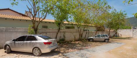 A residential area with two parked cars, a concrete wall, and a building with a tiled roof.