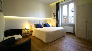 Una habitación de hotel con cama, una mesita, una silla y un ventanal con cortinas.