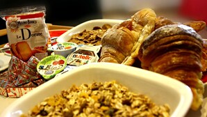 Una mesa de desayuno con diversos alimentos, incluyendo un croissant, un tazón de granola y una bolsita de galletas Le Dorate.