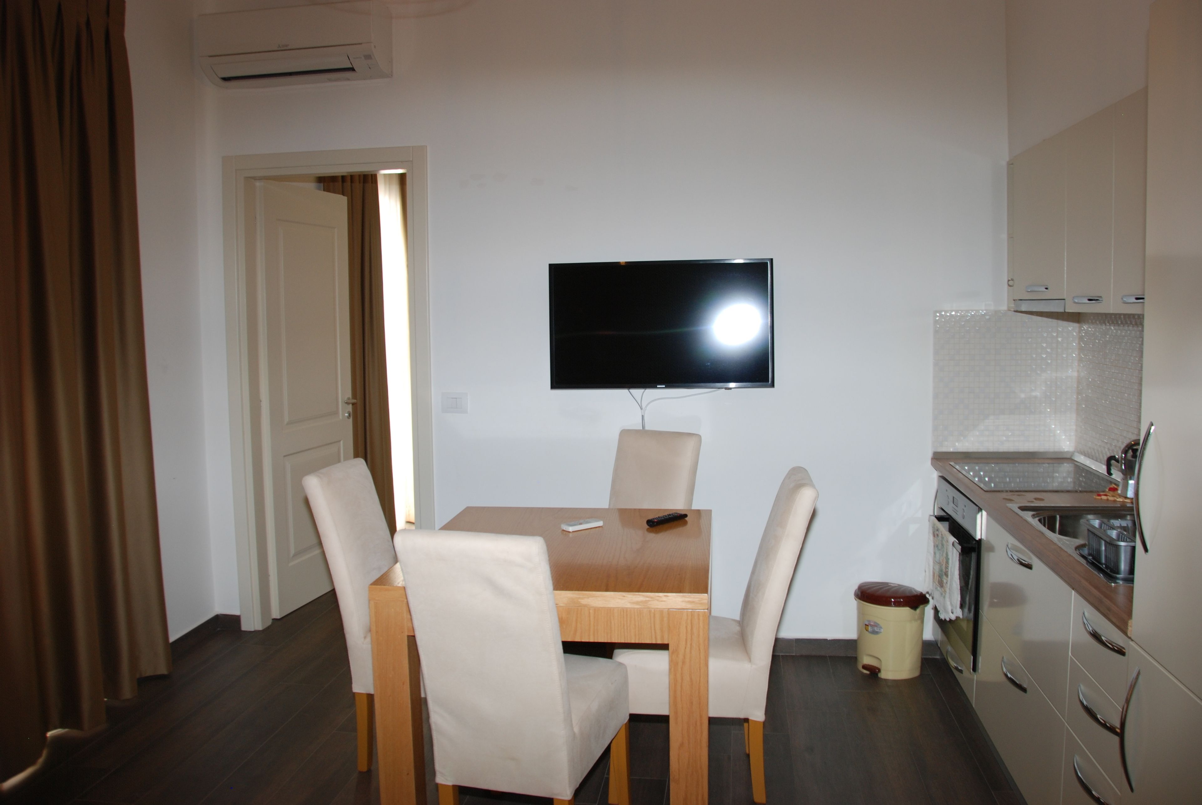 A small, modern kitchen with a dining area. There is a TV mounted on the wall above the dining table.