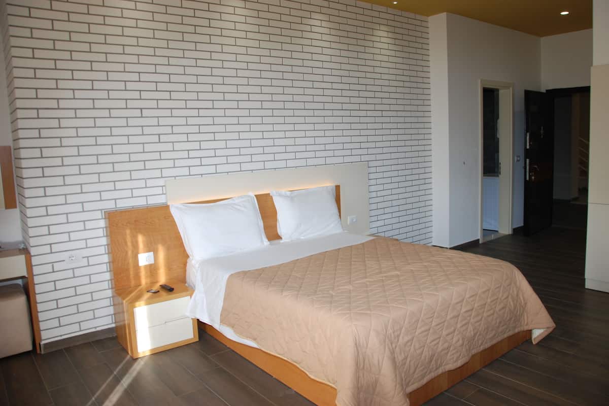 A modern hotel room with a brick-patterned wall, a wooden headboard, a beige quilted bedspread, and a nightstand with a remote control.