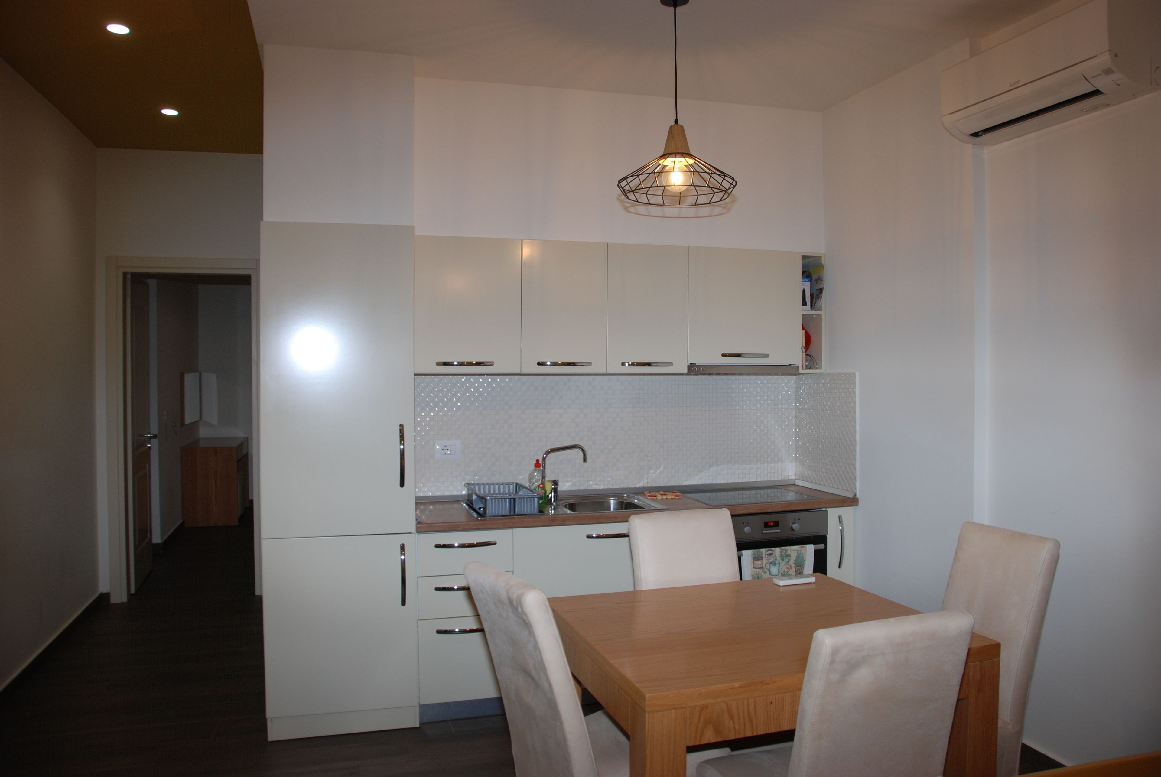 Een moderne keuken met witte kasten, een houten eettafel en een hanglamp.