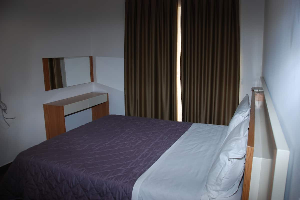 A neatly made bed with a purple and white bedspread, a wooden headboard, and a bedside table with a mirror.