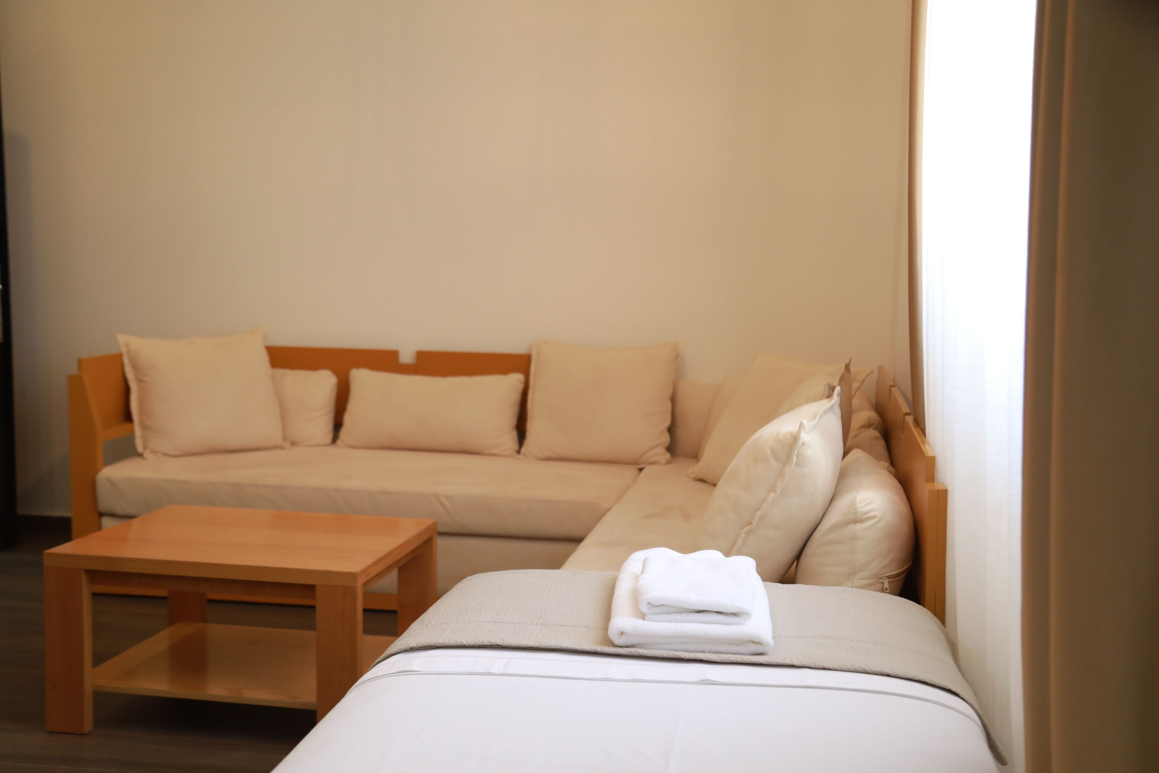 Una habitación de hotel moderna con una cama grande, una mesita de noche de madera y un sofá color beige.