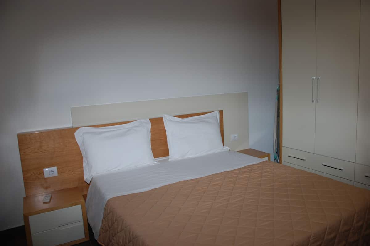A hotel room with a bed, a nightstand, a wardrobe, and a wall socket.