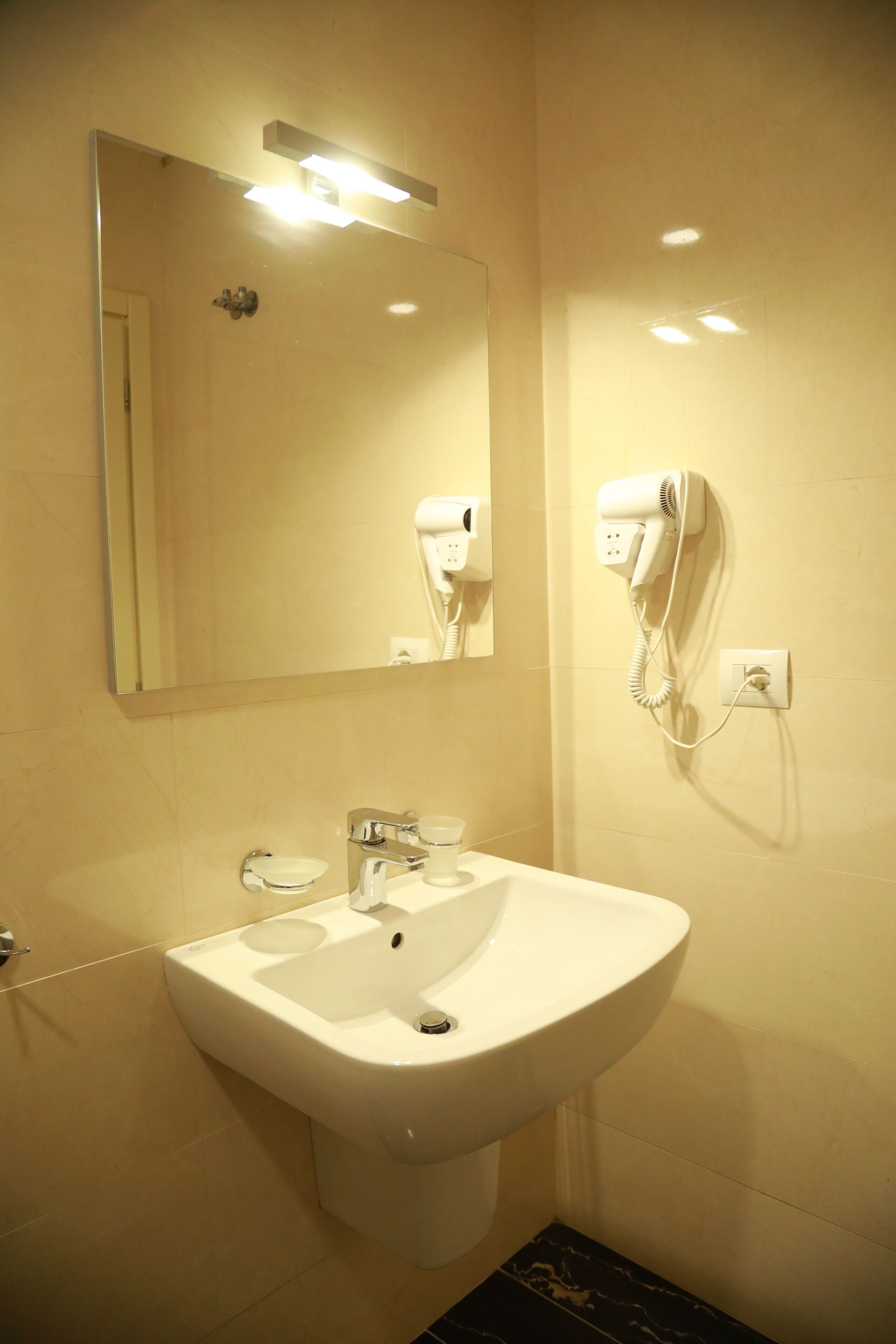 A bathroom with a sink, mirror, and hairdryer mounted on the wall.