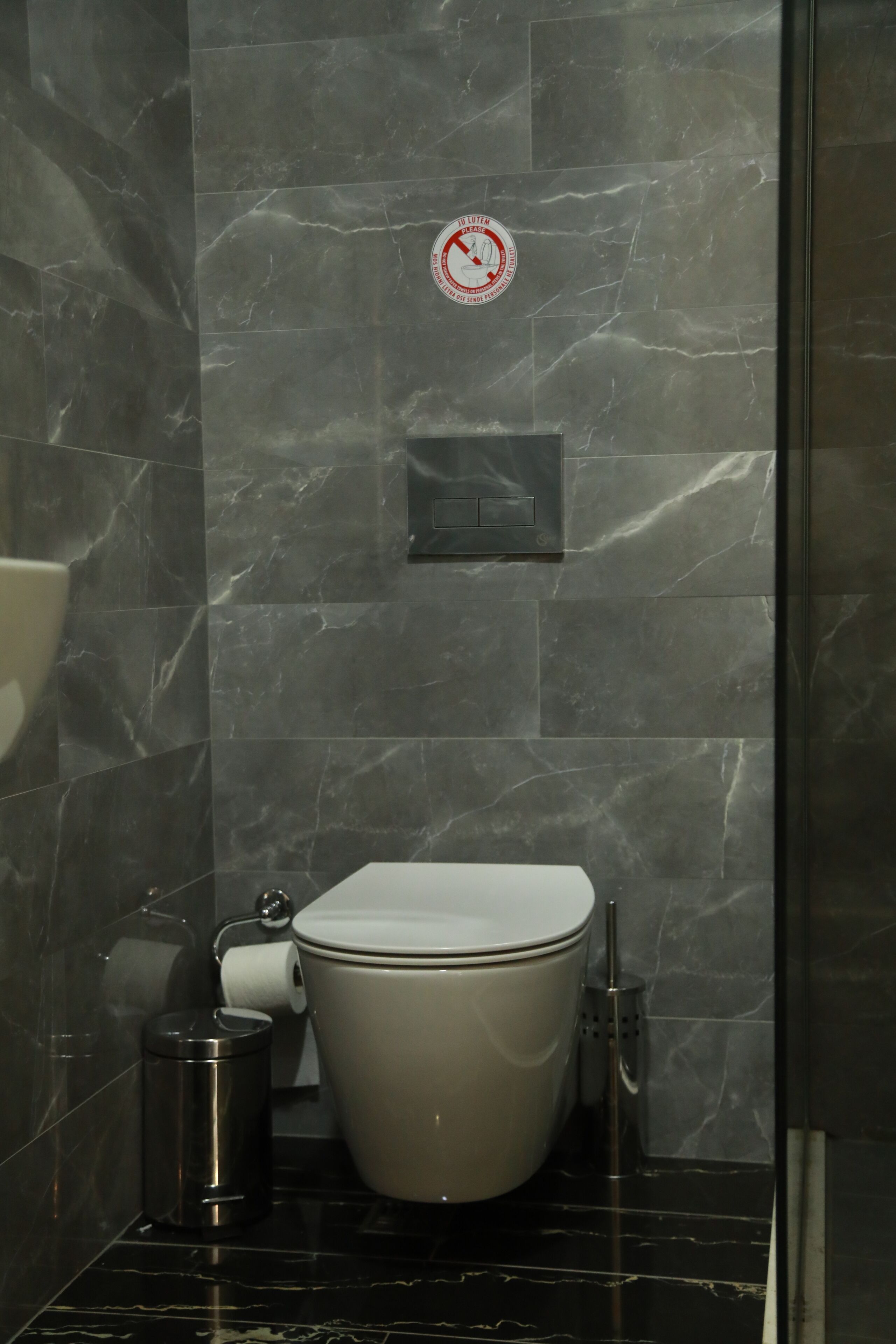 A bathroom with a toilet, a trash can, and a wall-mounted toilet paper dispenser.