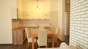Cozinha moderna com armários de madeira, uma mesa de jantar e cadeiras. Há uma pequena ilha com pia e uma luminária pendente.