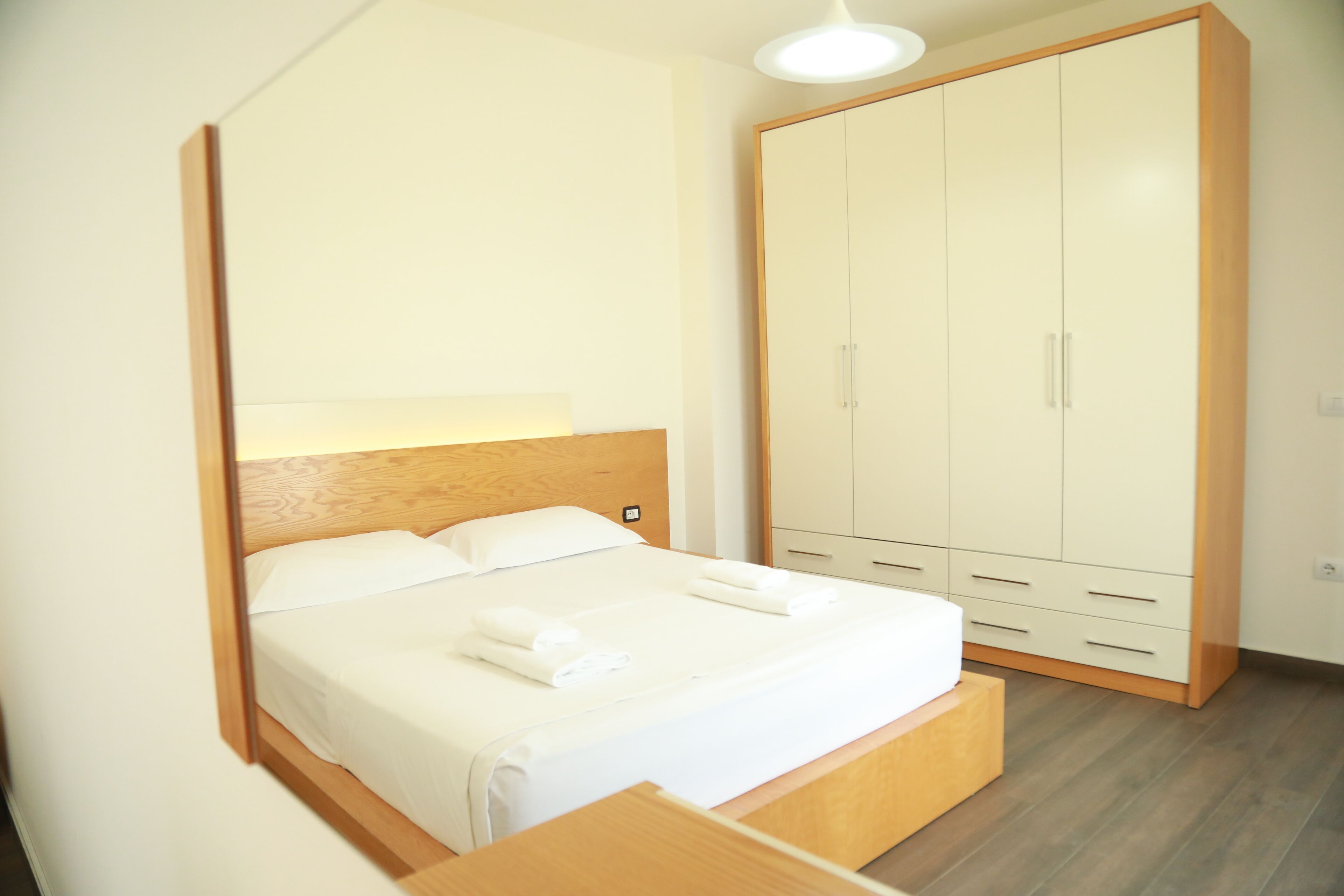 A bedroom with a bed, wooden headboard, white linens, a bedside table, and a wardrobe.