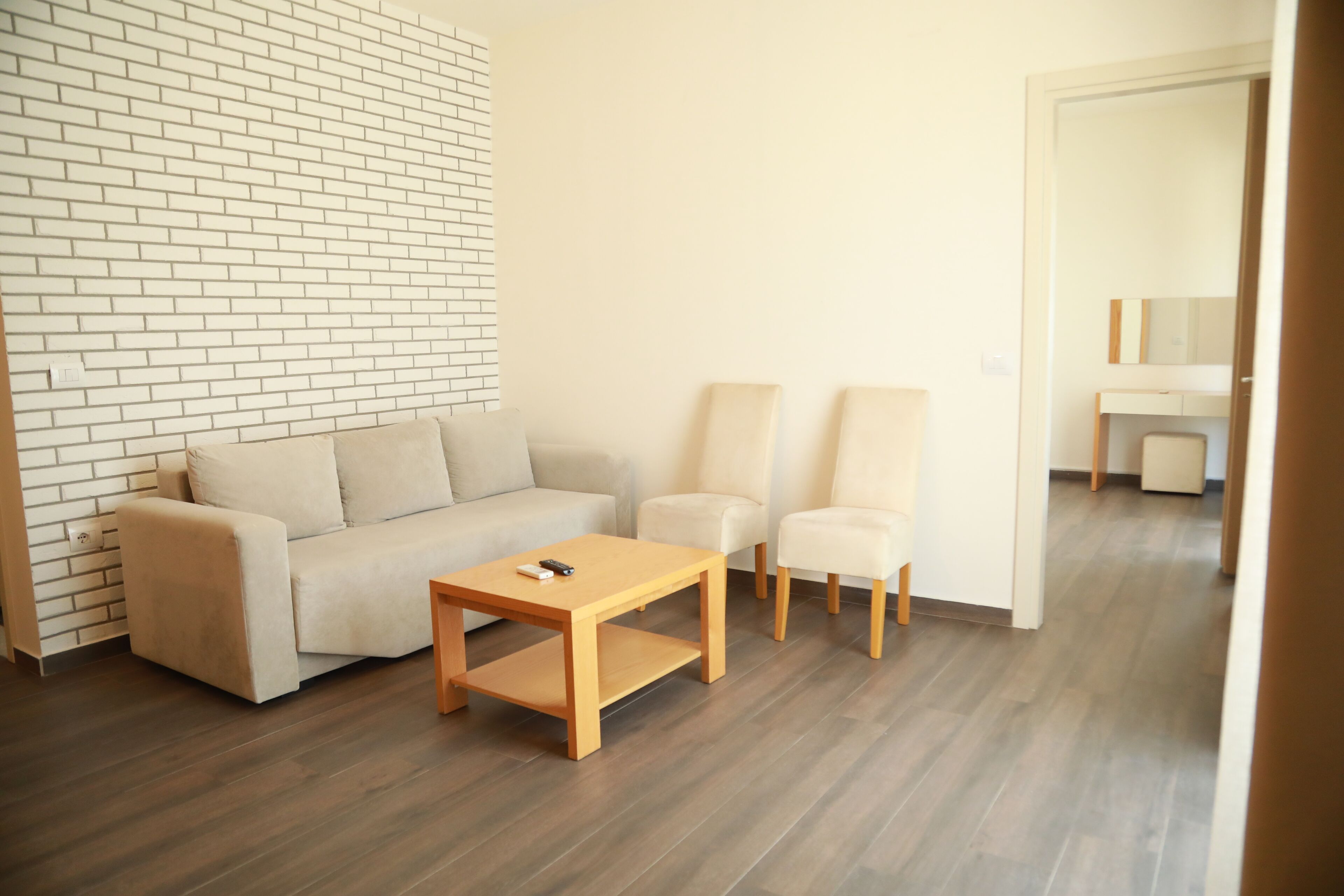 Ein modernes Wohnzimmer mit Backsteinwand, einer Couch, zwei Sesseln und einem Holztisch.