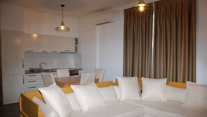 Uma sala de estar moderna com um sofá, uma mesa de centro de madeira e uma área de refeições com mesa e cadeiras.