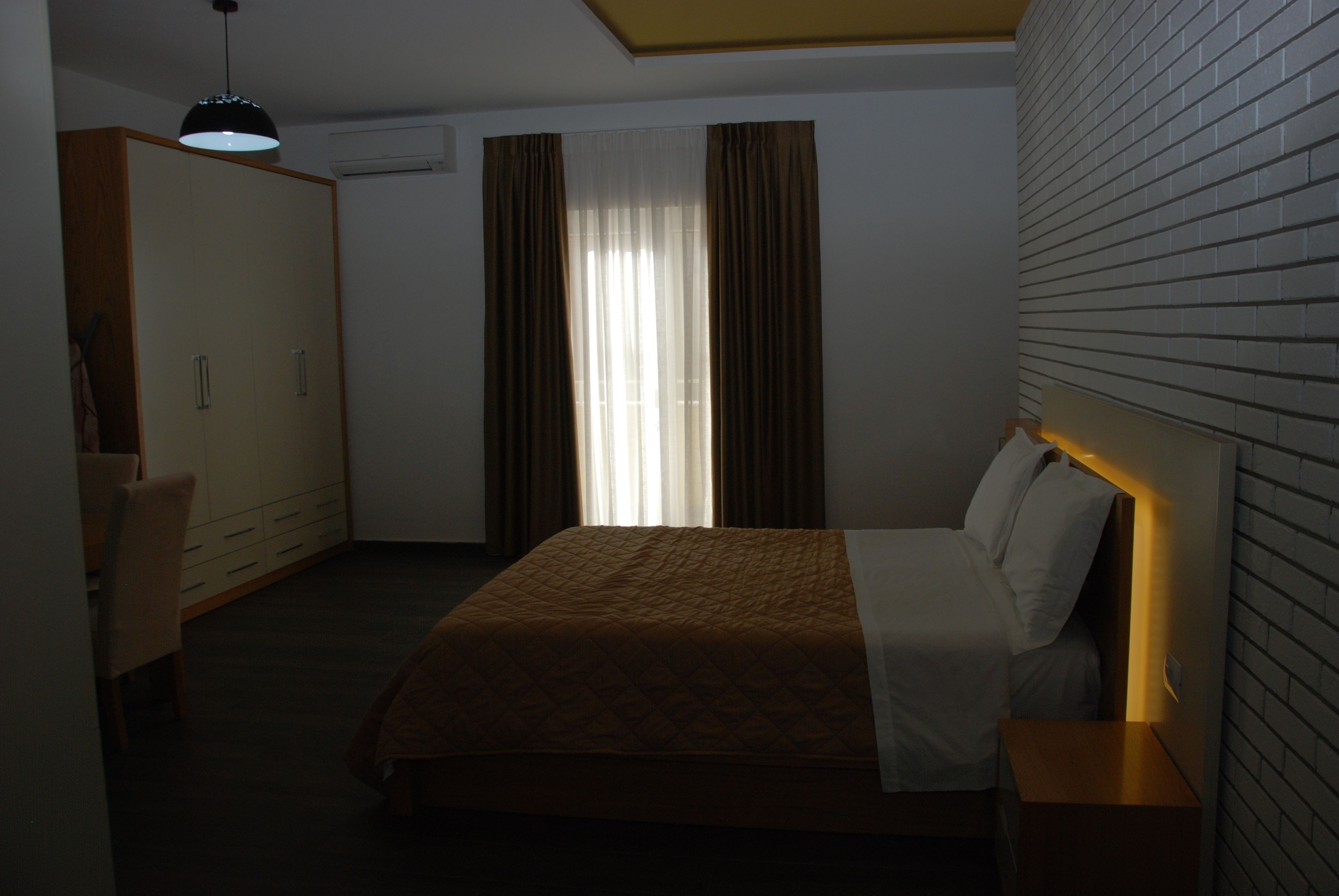 A hotel room with a bed, a wardrobe, a desk, and a hanging light fixture.