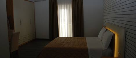 A hotel room with a bed, a wardrobe, a desk, and a hanging light fixture.