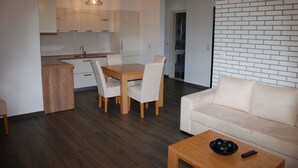 Uma sala moderna com sofá, mesa de jantar e cadeiras, cozinha com armários e piso de madeira.