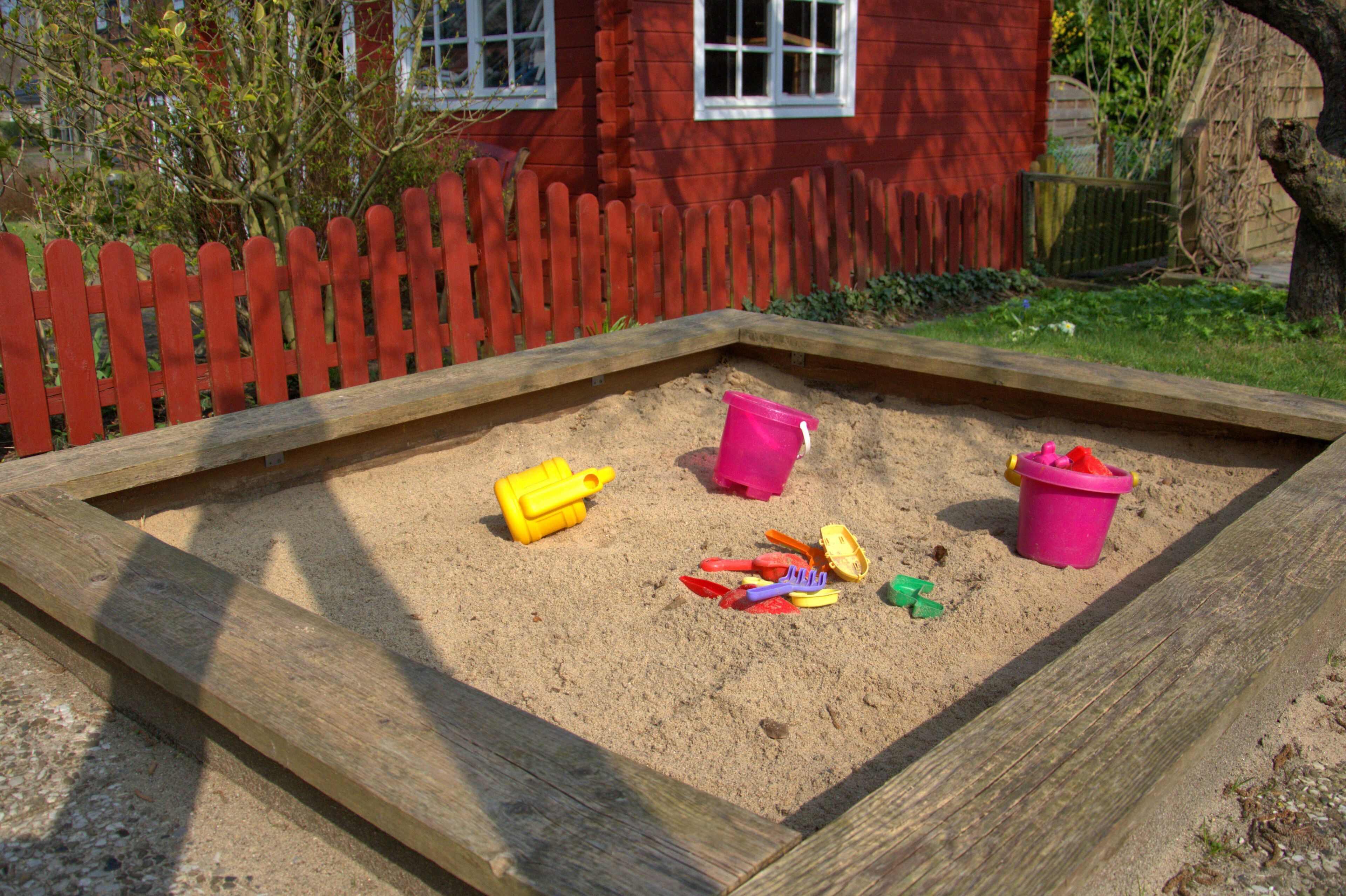 A sandbox with sand, a wooden border, and a red fence.