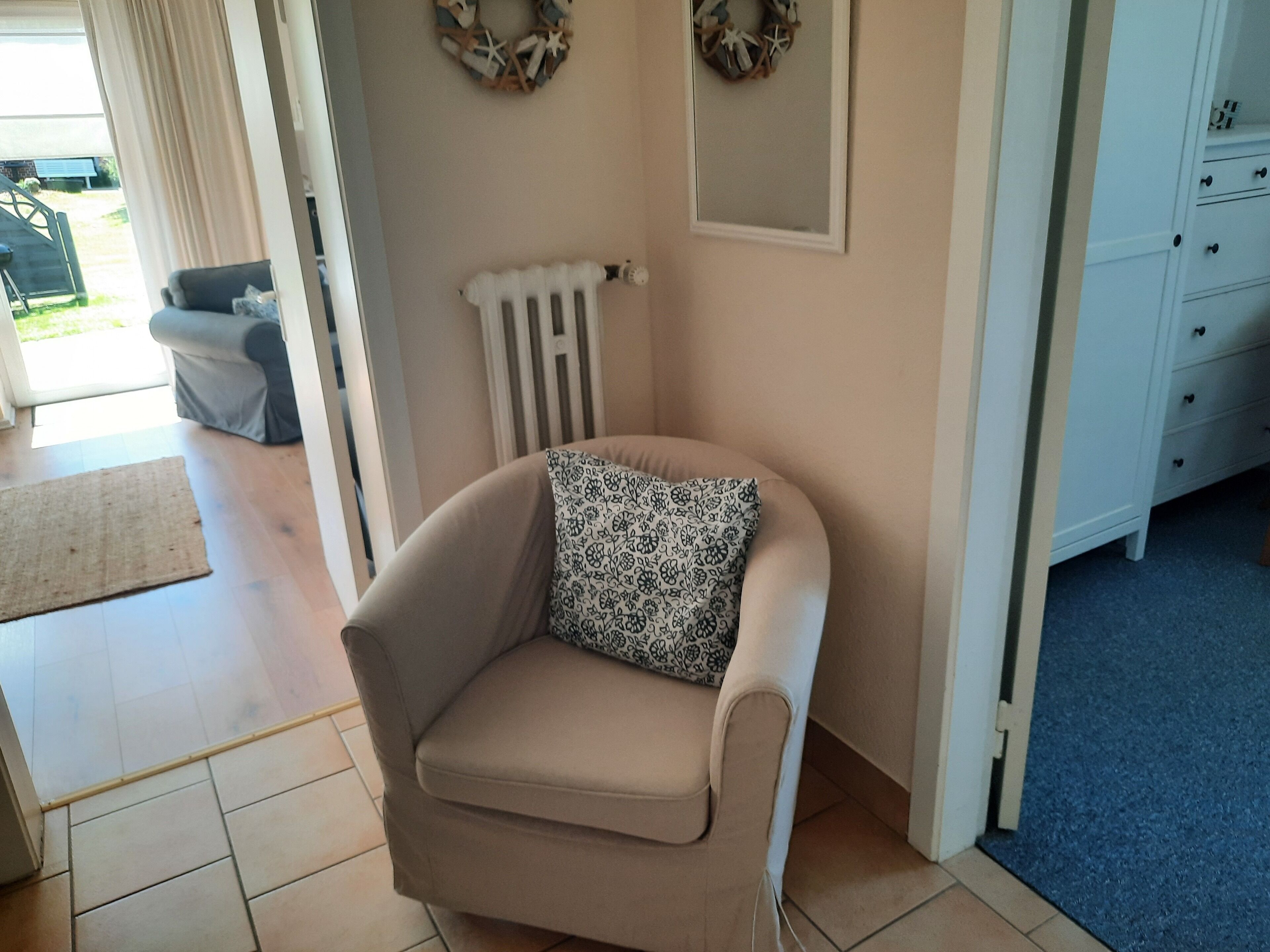 A corner room with a beige armchair, a radiator, a white dresser, and a blue carpet.