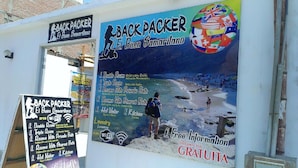 A signboard for Backpacker El Buen Samariano, listing amenities like double and triple rooms, private and shared baths, hot water, kitchen, laundry, and Wi-Fi. - El Buen Samaritano Backpackers - Hostel (Paracas)