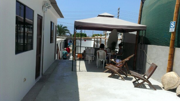 A narrow outdoor corridor with a covered seating area, a surfboard, and a sign indicating a service area. - El Buen Samaritano Backpackers - Hostel (Paracas)