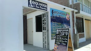 A building with a sign for 'BACKPACKER El Buen Samaritano' indicating a hostel with amenities like double rooms, triple rooms, private baths, and laundry services. - El Buen Samaritano Backpackers - Hostel (Paracas)