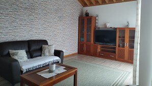 Un saló amb una paret de pedra, un sofà de cuir negre, un moble de fusta amb televisió i un sostre de fusta.