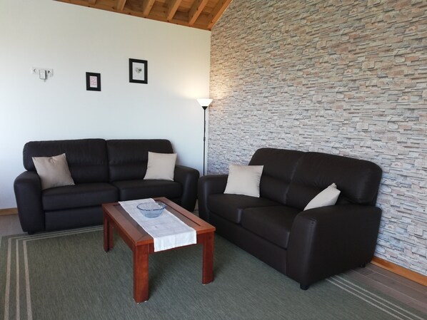 A living room with two black leather sofas, a wooden coffee table, and a stone-textured wall.